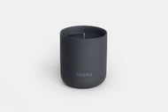 A matte black Ceramic Candle in a cylindrical container with THUMA on the front, displayed against a plain white background.