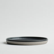 The Kinto - Ceramic Saucer Set features minimalist, round gray ceramic saucers with slightly raised edges and matte, dark gray interiors, shown on a plain white background.