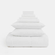 The Linen Complete Bedding Set, featuring folded white sheets, pillowcases, and pillows, is neatly arranged in a pyramid shape on a white background.
