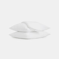 A folded Linen Sheet Set is draped over two stacked white pillows, all displayed against a plain white background.