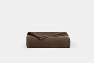 A neatly folded Cotton Ribbed Coverlet in textured brown is displayed against a plain light gray background.