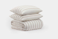 The Linen Stripe Duvet Cover Set by CULTIVER features two white pillows with thin brown stripes stacked on a matching rolled-up comforter, all displayed against a plain white background.