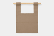The Leather Bed Sleeve is a tan, rectangular leather organizer with a large pocket, shown draped over a light wooden rod against a white background.