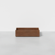 The Classic Underbed Drawer, a rectangular low wooden box with smooth sides, sits on a light gray floor against a plain white background.