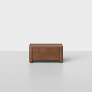 The Essential Nightstand, 24″ features a low-profile design crafted from walnut wood, with a single drawer, rounded corners, and short legs, showcased against a minimal white background.