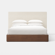 The Essential Storage Bed + Upholstered Headboard features a sleek wooden base and a white upholstered headboard, accented with neatly arranged white pillows and bedding, all set against a plain white background.