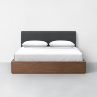 The CL Test - Essential Bed Main Product features a dark gray upholstered headboard, white bedding and pillows, and a rectangular wooden frame set against a plain white wall and light gray floor.