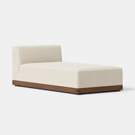 Essential Armless Chaise featuring a cream-colored upholstered seat and backrest, set on a low, rectangular wooden base, displayed against a plain white background.