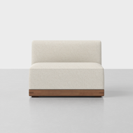 The Essential Armless Chair features cream-colored upholstery and a wooden base, shown on a light gray floor against a plain white background.