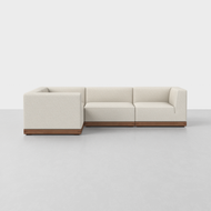 The Essential L Sectional is a modern L-shaped sofa featuring light beige upholstery and a wooden base, displayed against a plain white background on a light gray floor.