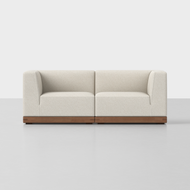The Essential Modular Sofa is a modern beige upholstered loveseat featuring clean lines and a wooden base, shown against a plain white background.