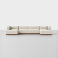 The Essential U Chaise Sectional is a modern, low-profile sofa with off-white upholstery and a wooden base, arranged in an L-shape against a plain white background and floor.