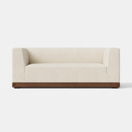 The Essential Sofa, 72″, a modern cream-colored loveseat with a low back and armrests, upholstered in fabric and set on a wooden base, sits against a plain white background.