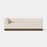 The Essential Sofa, 84″, is a modern, cream-colored sofa with square arms and a wooden base, set against a plain white background.
