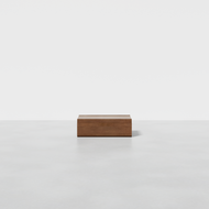 The Nest Nightstand Low, a rectangular wooden piece, sits centered on a smooth light gray floor against a plain white background in a minimalist, empty setting.
