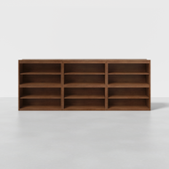 The Nest Shelving is a large, rectangular wooden bookshelf with three columns and three rows of open shelves, shown against a plain white background on a light gray floor.