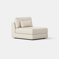 The Signature Armless Chair features cream textured fabric, thick seat and back cushions, and a matching lumbar pillow on a low black base, shown against a white background.
