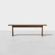 The Pillar Bench + Cushion features a minimalist design with a rectangular wooden seat and four straight legs, shown against a plain white background.
