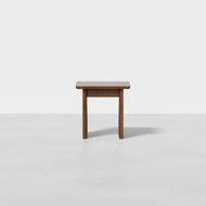 A compact Pillar Stool with four legs sits on a smooth light grey floor in front of a plain white background.