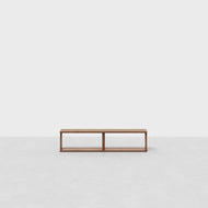 The Pillar Media Console, featuring a minimalist rectangular design with an open frame, sits on a light gray floor against a plain white background.