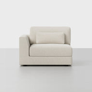 The Custom Signature Sectional features a modern, off-white upholstered armchair with a single left armrest and matching rectangular cushion, displayed on a light gray floor against a white backdrop.