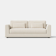 Signature Sofa, 84″, shown in a cream color against a plain white background, features two back cushions and two rectangular throw pillows. Its minimalistic design is characterized by clean lines and a boxy shape.
