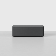 The Signature Storage Bench, a rectangular dark gray upholstered ottoman, sits on a light gray floor against a plain white background.