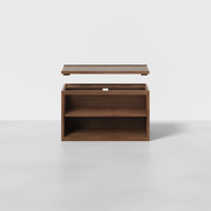 The Nest Shelf is a wooden rectangular storage box featuring an open front shelf and a removable lid above it, shown on a light gray floor against a plain white background.