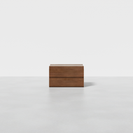 The Nest Nightstand, a sleek and modern wooden storage box with clean lines, stands on a smooth light gray floor against a plain white background.